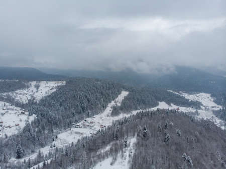 Aerial view of a Mountain Village with Hills Covered in Snow and Pine Forest in Winter. Yaremche, Ukraine. Flying over the snowy hills and wooden small houses. Countryside, fir tree. Drone viewの写真素材