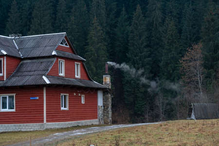 White smoke from the chimneys of Accurate Wooden houses in a mountain village in Autumn on a background of forest and mountainsの写真素材