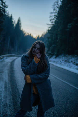 Beautiful Young Woman On the Dark Forest Road at Winter. Twilights, Car Lights on Backgroundの写真素材