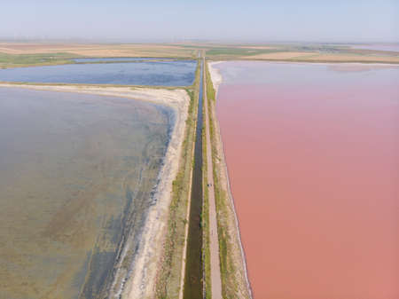 Aerial Drone Shot of a Dam with asphalt Road between Estuaries with Different color of Water. Pink Orange Lake and Green or Blue lake aside a road in Ukraine. Lake Sivashの写真素材