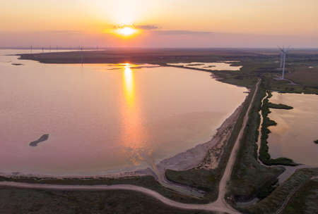 Aerial Drone Shot of colorful pink lake at sunset time with wind turbines farm on background. Cinematic landscape view picturesque margenta water in Ukraine, Kherson Oblast, lake Syvashの写真素材