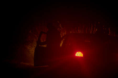 Silhouette of a man, Going out From the Car on a Curb at Night Road at Misty Weatherの写真素材