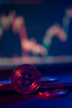 Bitcoin Coins are standing on laptop in neon Light with a Chart on a screen at background