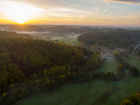 Aerial drone Sunrise view Above autumn colored forest and Valleys in Luxembourg, covered in morning fogの写真素材