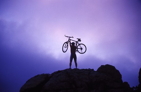 a woman holds her bicycle overhead in victoryの写真素材