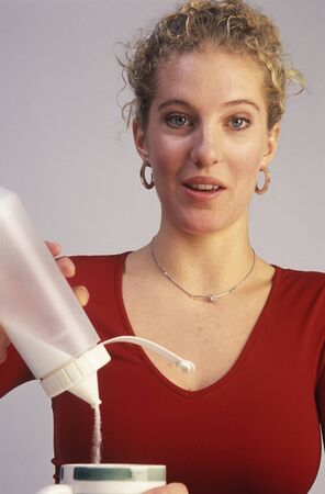 A young blond woman pours sugar into her coffee cupの写真素材