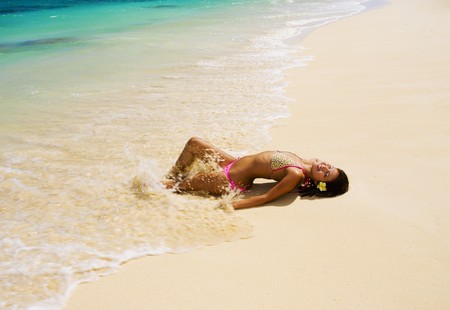 a beautiful young Polynesian girl in a pink bikini lying on a Hawaii beachの写真素材