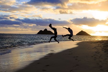 silhouette of twin brothers with drum and guitar leaping in the air at sunrise on a hawaii beachの写真素材