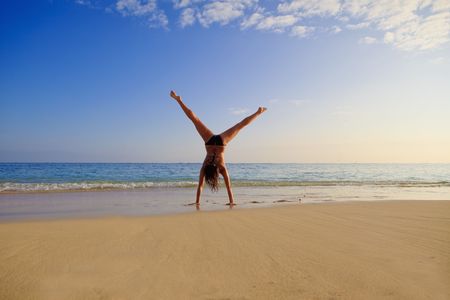 young woman doing a cartwheel on a hawaii beachの写真素材