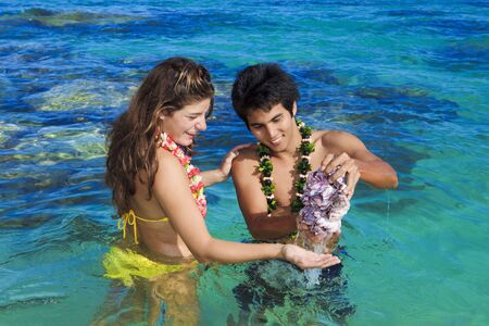 island man shows seashells to a young woman in the ocean in hawaiiの写真素材