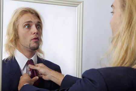 young man in a mirror getting his tie adjusted by his reflectionの写真素材