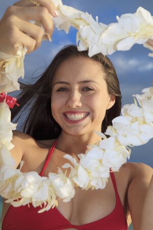 beautiful young woman in a red bikini and a ginger lei on the beach at lanikai at sunrise, offers a leiの写真素材