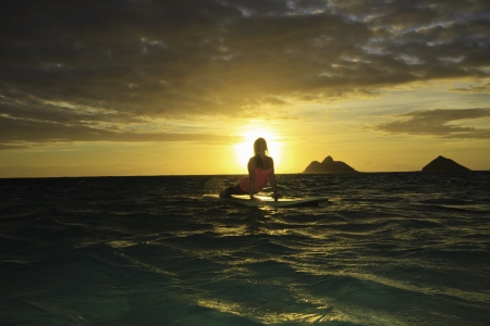 woman doing yoga on her paddle board at sunrise
