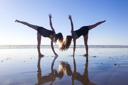two girls doing yoga on the beach
