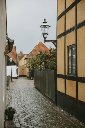Detail of street lamp with ornaments hanging on yellow wall of old house in empty street, with granite road, oldest Denmark village Ribe with overcast sky in the backgroundの写真素材