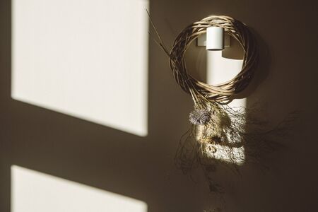 Enlightened wicker wreath with dry flowers hanging on white wall with shadows of the frame of the window - lifestyle sceneの写真素材