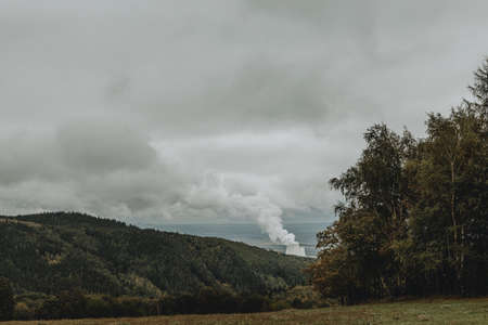 To the sky rising steam from cooling towers of power plant hiding in valley of Ore mountains in Czech republic during the cloudy autumn dayの写真素材