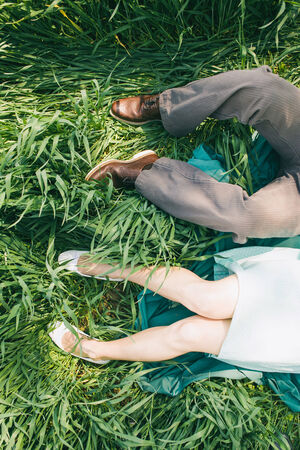 Laying couple in the high grass, top perspective, only legs, engagement photo, before wedding, picnic, sunny day, romantic photo, without face, gilr with turquoise dress, vintage colorの写真素材