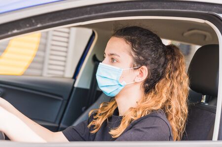 New normal. Female driver with a medical face mask driving a car with a passenger. Health...