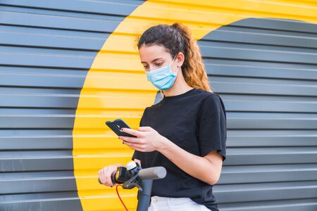 New normal. Young girl with a mask using an electric scooter. Woman using electric and ecological...