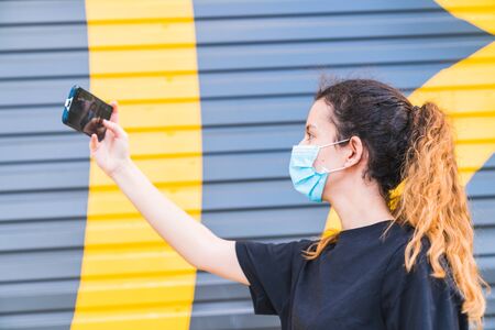 Teenager making a selfie on the street wearing a mask. Young woman protected by a mask. Selfie with mask. Human life in Social distance. Safety and pandemic concept. Social distance. New normal.の写真素材
