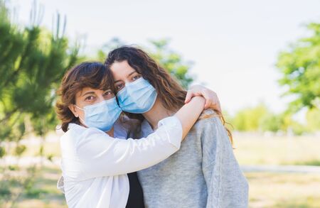 Social distance. Mother and daughter with a protective mask hugging in a park. Ending the Coronavirus Pandemic. Coronavirus devices. Social distancing. Protection against pandemic. End of the pandemicの写真素材