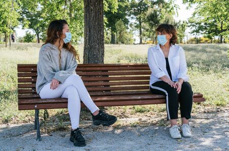 Social distance. Mother and daughter in social distance sitting on a park bench. Pandemic....