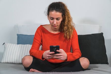 Teenager using the smartphone in his living room. Young student using the smartphone. Girl using the...