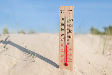 Wooden celsius and fahrenheit scale thermometer in the sand. Ambient temperature plus 3 degrees. Hot summer dayの写真素材