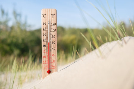 Wooden celsius and fahrenheit scale thermometer in the sand. Ambient temperature plus 18 degrees. Hot summer dayの写真素材