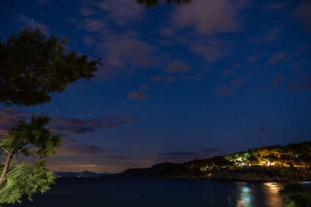 Night view of the very calm sea on the shore with the illuminated town in the backgroundの写真素材