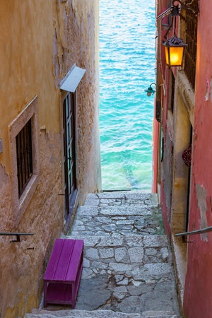 Beautiful narrow staircase between old buildings leading straight to the seaの写真素材