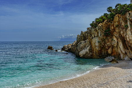 A beautiful view of the calm sea and the sandy beach surrounded by rocksの写真素材