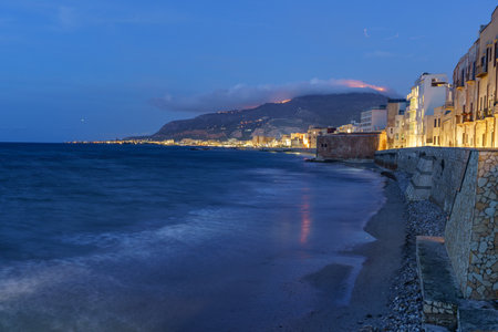 A beautiful seaside small town lit up at night, built right next to a calm sea.の写真素材