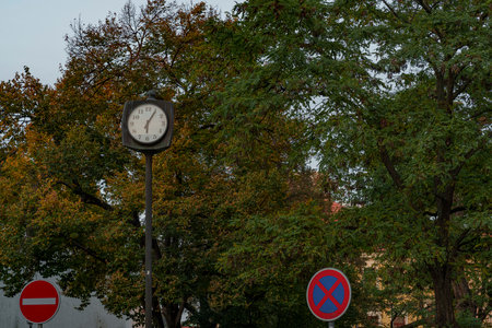 An old analog clock against the backdrop of an autumn tree and road signs.