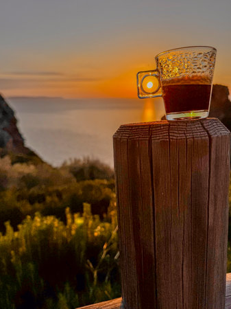 A cup of coffee against the backdrop of the setting sun over the sea in the mountainsの写真素材