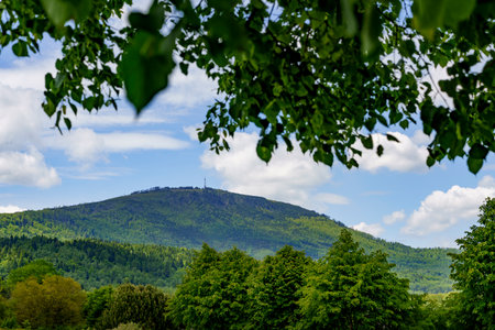 view of mount Skrzyczne topped with a radio-television transmitter under blue sky with clouds, framed by lush green leaves and branchesの写真素材