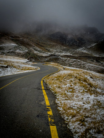Winding road with yellow line cut through snowy, misty Carpathians, fog-shrouded peaks and wild slopes.の写真素材