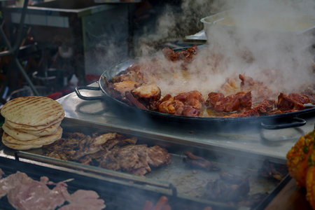 Slices of grilled and roasted meat sizzle in a pan over high heat, surrounded by steam and stacked...