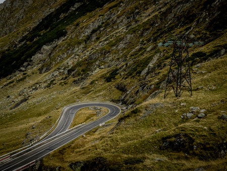 A single winding curve hugs the grassy slope, watched over by a solitary electricity pylon.の写真素材