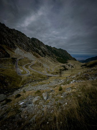 A series of sweeping curves cut through a desolate valley, beneath overcast skies and rugged slopes.の写真素材