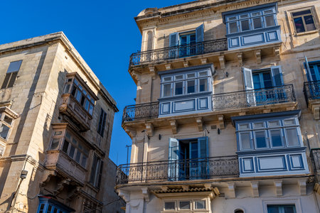 Traditional painted wooden balconies and ornate wrought iron railings decorate sunlit Mediterranean limestone buildings.の写真素材