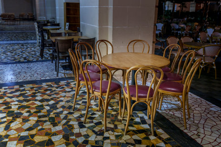 Round wooden table with classic cafe chairs stands on patterned tiles in an open-air seating area at...