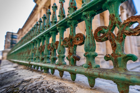 Close low-angle view of weathered green wrought-iron railing with rust textures beside limestone...