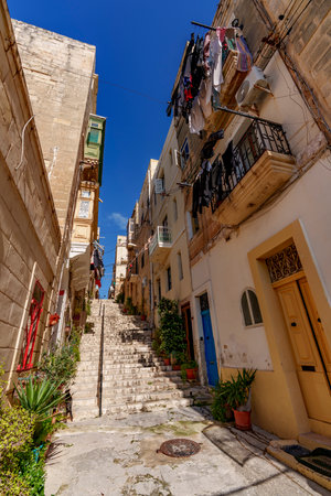 Narrow stair street rises between warm stone facades with colorful balconies, potted plants and clotheslines.の写真素材