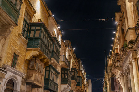 Historic limestone buildings lined with enclosed wooden balconies rise against a dark sky along an illuminated street.の写真素材