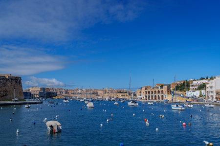 Daytime view across calm water dotted with buoys and small boats toward limestone waterfront and marinas.の写真素材