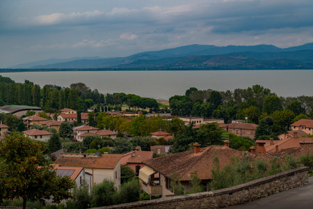 Village with terracotta rooftops overlooking a large lake, distant mountains, cloudy sky, lush green.の写真素材