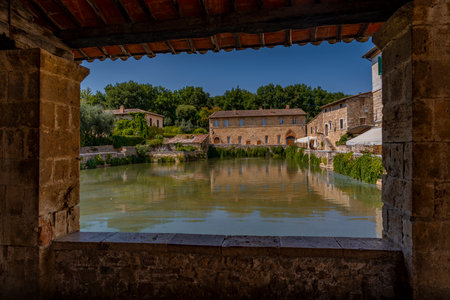 Old stone window frames tranquil pool reflecting historic Tuscan buildings and summer trees.の写真素材