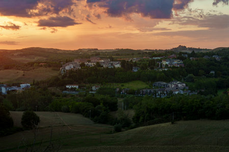 Golden sunset sky lights Tuscan countryside, peaceful village nestled in green hills.